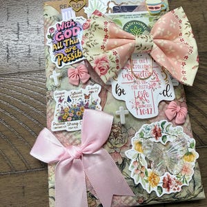 May include: A rectangular decorative item featuring a floral pattern, adorned with a large pink satin bow, a fabric bow with a rose print, and various stickers including text that reads With GOD All Things are Possible and Proverbs 10:17.
