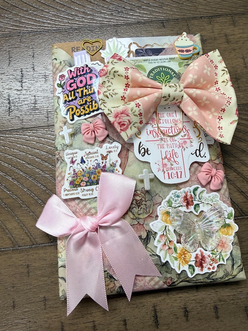 May include: A rectangular decorative item featuring a floral pattern, adorned with a large pink satin bow, a fabric bow with a rose print, and various stickers including text that reads With GOD All Things are Possible and Proverbs 10:17.