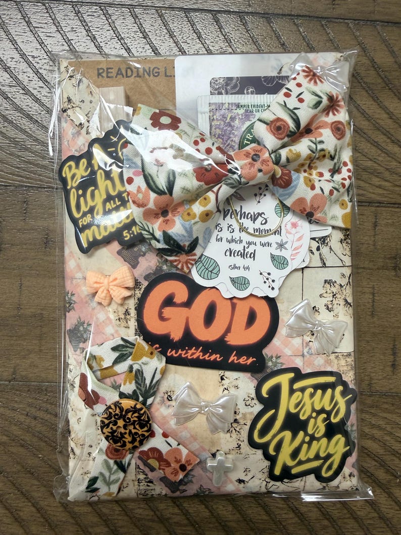 May include: A packaged set featuring a floral fabric bow, stickers with text including "Be the light," "God is within her," and "Jesus is King," a small peach-coloured bow, a black and gold patterned button, and a small white cross charm.