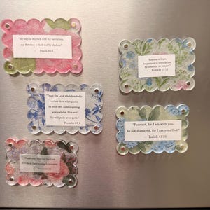 May include: Five rectangular magnets with scalloped edges and floral patterns. Each magnet features a white paper insert with printed scripture verses including Psalm 62:6, Romans 12:12, Proverbs 3:5-6, Isaiah 41:10, and Isaiah 40:31. The magnets are clear.