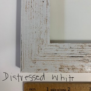 K&ouml;nnte beinhalten: Nahaufnahme eines wei&szlig;en, verwitterten Holzbildrahmens mit einem Lineal, das 2,5 cm misst. Der Rahmen ist wei&szlig; lackiert mit einer verwitterten Oberfl&auml;che, was ihm einen rustikalen Look verleiht.