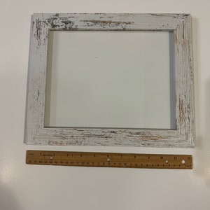 May include: White wooden picture frame with a distressed finish. The frame is 12 inches wide and 16 inches tall.