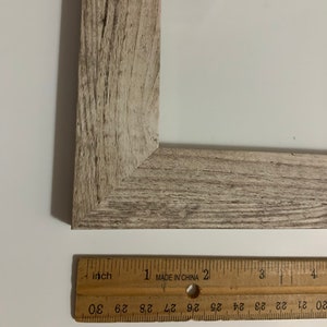 May include: A close-up of a wooden picture frame with a light brown, weathered finish. The frame is 4 inches wide and has a beveled edge. The word "Burlywood" is written below the frame.