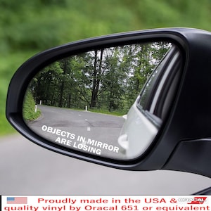 May include: A car side mirror with the text "OBJECTS IN MIRROR ARE LOSING" in white. The mirror reflects a road winding through a forest. The sticker is made of quality vinyl.