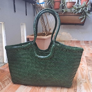 Könnte beinhalten: Eine dunkelgrüne gewebte Tragetasche mit geflochtenen Griffen. Die Tasche hat eine rechteckige Form mit einer breiten Öffnung und einem strukturierten, korbartigen Gewebe. Die Griffe sind dick und geschlungen.