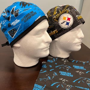 May include: Two surgical caps, one black with a Pittsburgh Steelers logo and the text "Pittsburgh Steelers", and one blue with a Carolina Panthers logo and the text "Carolina Panthers". A black fabric with a Carolina Panthers logo is in the foreground.