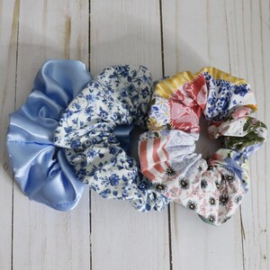 Puede incluir: Tres scrunchies para el pelo, uno de sat&eacute;n azul y dos de tela estampada. Los scrunchies estampados tienen un dise&ntilde;o floral en tonos azules, rosas y amarillos.