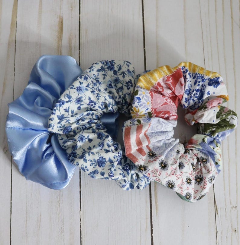Puede incluir: Tres scrunchies para el pelo, uno de sat&eacute;n azul y dos de tela estampada. Los scrunchies estampados tienen un dise&ntilde;o floral en tonos azules, rosas y amarillos.