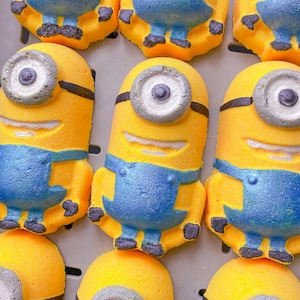 Könnte beinhalten: Ein Set mit zehn gelben Badebomben in Form des Minions aus dem Film Ich - Einfach unverbesserlich. Die Badebomben haben blaue Latzhosen, schwarze Augen und ein weißes Lächeln.