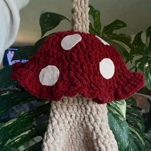 Puede incluir: Un bolso de crochet hecho a mano con forma de seta en rojo burdeos con lunares blancos y un tallo beige. El bolso se sujeta por un asa beige. Un accesorio caprichoso.