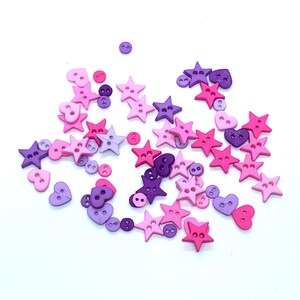 Peut inclure: Un assortiment de boutons décoratifs roses et violets. Les boutons sont en forme d'étoiles, de cœurs et de cercles. Les boutons sont dispersés sur un fond blanc.