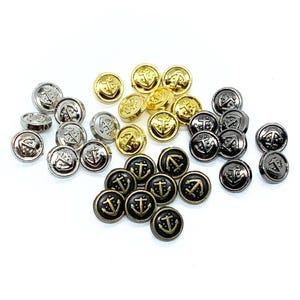 Peut inclure: Plusieurs boutons ronds de différentes couleurs métalliques, argent, or et noir. Chaque bouton est orné d'une ancre. Les boutons sont dispersés sur une surface blanche, soulignant leur thème nautique. Idéal pour la couture.