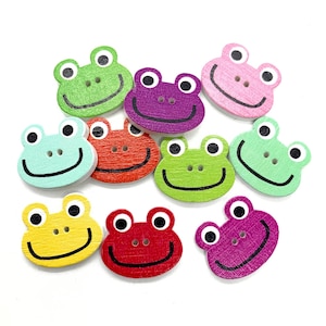 Peut inclure: Un assortiment de boutons en bois en forme de grenouille, de différentes couleurs : vert, violet, rose et jaune. Chaque bouton présente un visage souriant, des yeux noirs et deux trous pour les boutons. Ces boutons décoratifs sont parfaits pour les travaux manuels et la couture.