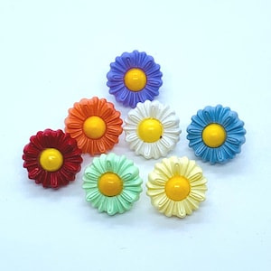 Peut inclure: Assortiment de sept boutons en forme de marguerite de couleurs vives avec des centres jaunes. Les boutons sont dans des tons de rouge, orange, vert clair, blanc, bleu clair et violet.