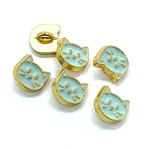May include: Six gold-coloured cat face buttons with a light blue enamel finish. The buttons have a raised design and are perfect for adding a touch of whimsy to any project.
