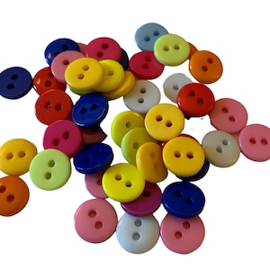 Peut inclure: Un assortiment de boutons ronds colorés, dans des tons de bleu, jaune, rose et blanc. Chaque bouton comporte deux trous pour la couture. Les boutons sont dispersés sur un fond blanc.