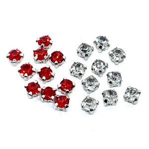 Peut inclure: Un assortiment de petits pierres précieuses rondes. Certaines sont d'un rouge vif, tandis que d'autres sont claires et scintillantes. Chaque gemme est sertie dans une base métallique argentée, créant un contraste de couleurs et de textures. Les gemmes sont dispersées sur un fond blanc.
