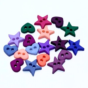May include: A selection of wooden buttons in star and heart designs. The buttons are in a variety of colours, including pink, purple, blue, green, and orange. Each button has two holes for sewing.