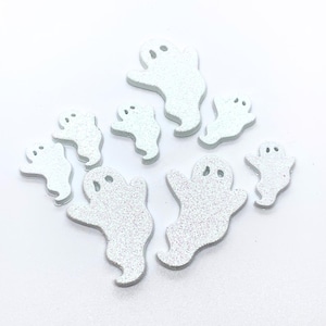 Peut inclure: Un ensemble de huit formes de fantômes en paillettes blanches. Les fantômes sont de tailles et de formes variées, certains ayant une forme de fantôme plus traditionnelle et d'autres une forme plus arrondie.