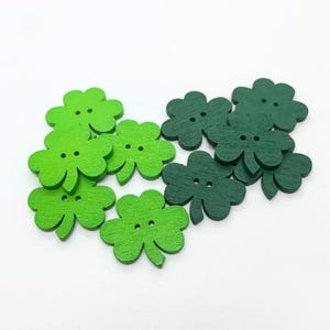 May include: A collection of green and dark green wooden shamrock buttons. The buttons are shaped like four-leaf clovers and have two holes each.