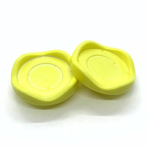 May include: Two yellow ceramic coasters with a slightly wavy edge and a raised centre.