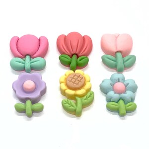 May include: Six colourful flower-shaped buttons with a variety of designs, including a pink tulip, a red tulip, a yellow sunflower, a purple flower, and two blue flowers.