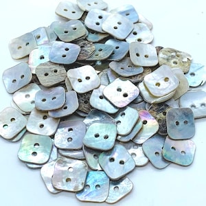 May include: A pile of iridescent white shell buttons with two holes each. The buttons are square shaped with rounded corners.
