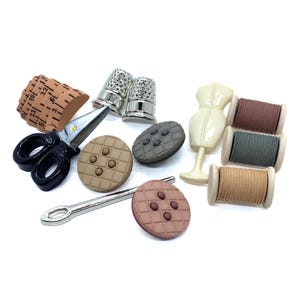 May include: A selection of sewing embellishments, including scissors, thimbles, buttons, a dress form, and spools of thread. The buttons are in shades of brown and pink. The scissors have black handles. The thimbles are silver.