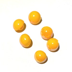 May include: A group of seven yellow round beads, some with a slight shine, on a white background.