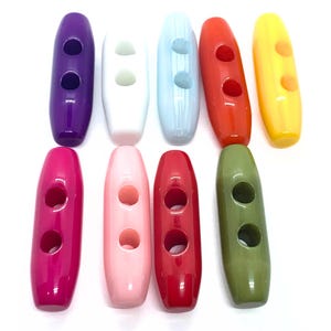 May include: A selection of oval buttons in a range of colours: purple, white, light blue, red, yellow, pink, light pink, dark red, and green. Each button has two holes for sewing.