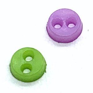 以下が含まれることがあります： 2つの小さくて丸いボタン。1つは鮮やかな緑色、もう1つはソフトな紫色です。各ボタンには縫い付け用の穴が2つあります。ボタンは滑らかな素材、おそらくプラスチック製で、白い背景に配置されています。