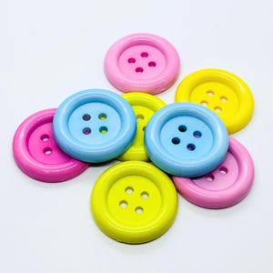 May include: A collection of six colourful buttons in shades of blue, yellow, and pink. Each button has four holes and a raised centre.