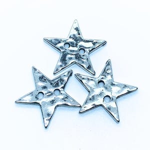 May include: Three silver star-shaped buttons with a hammered texture. Each button has two holes.