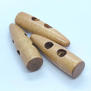 May include: Three wooden toggle buttons, each with two holes. The buttons are light brown and have a smooth, rounded finish.