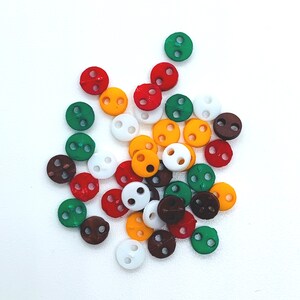 Peut inclure: Assortiment de boutons en plastique colorés avec deux trous chacun. Les boutons sont dans des tons de rouge, vert, jaune, blanc et marron.