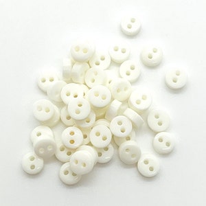 May include: A pile of white plastic buttons with two holes each. The buttons are small and round.