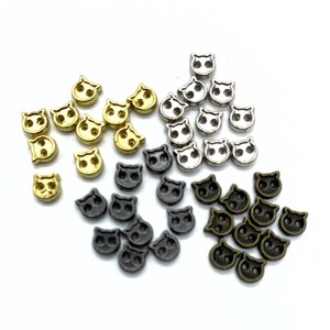 Peut inclure: Plusieurs petits ornements métalliques en forme de chat, de couleurs or, argent, noir et bronze. Ces pièces décoratives comportent deux trous pour être fixées. Les visages de chat sont détaillés et uniformes.