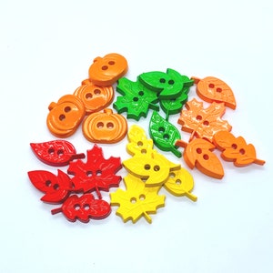May include: Assortment of wooden buttons in autumnal colours, including orange, green, and red. The buttons are shaped like leaves and pumpkins.
