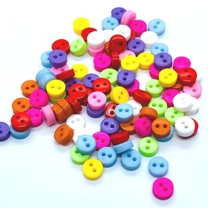 Peut inclure: Un grand assortiment de boutons en plastique colorés dans différentes nuances de rose, bleu, vert, jaune, orange et rouge. Les boutons sont petits et ont deux trous.