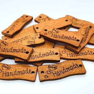 May include: A pile of wooden tags with the word "Handmade" and a heart with the word "Love" engraved on them. The tags have two holes for string or ribbon.