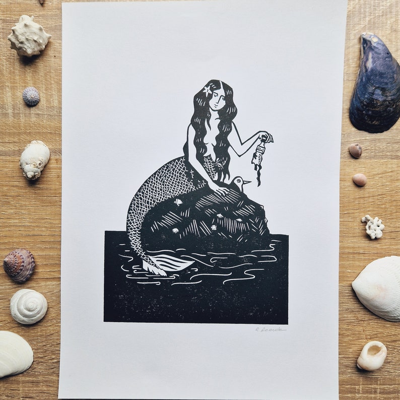 A mermaid on a rock, holding a plastic bottle that has washed up. Linocut print