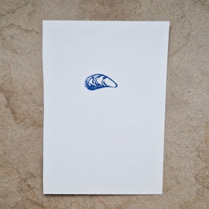 May include: A blue ink stamp of a single seashell on a white background.