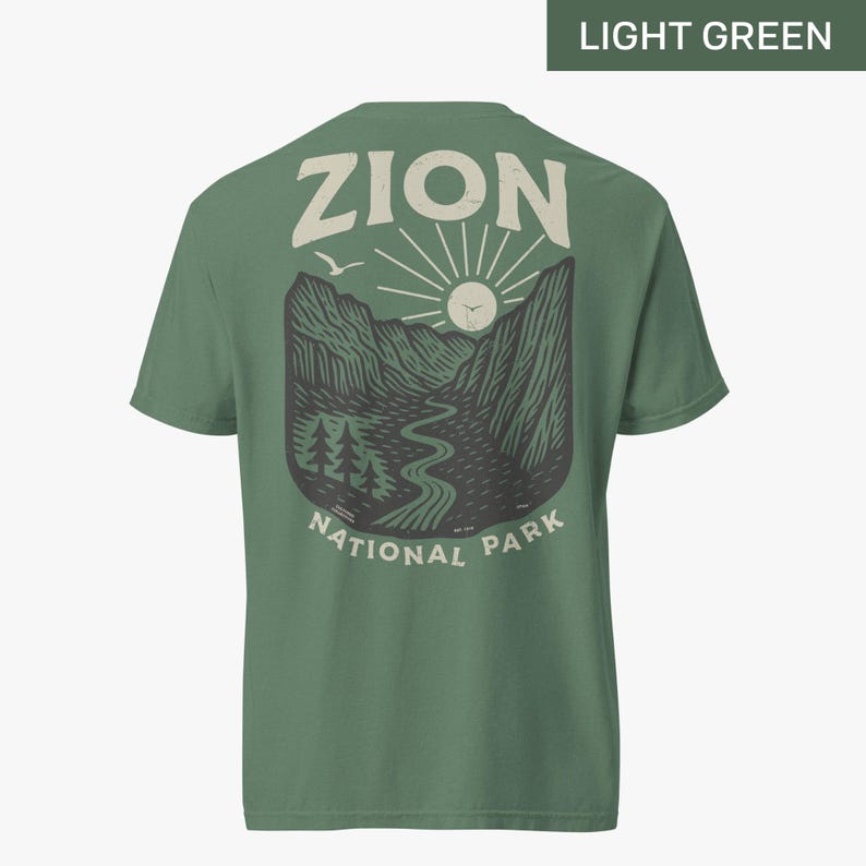 May include: A light green t-shirt with a vintage-style graphic of a mountain landscape with the text "Zion National Park" and the word "Zion" in a large font above the graphic.