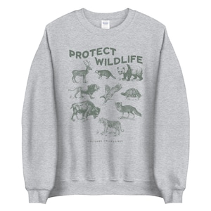 May include: A heather gray sweatshirt with a green graphic that says "PROTECT WILDLIFE." The graphic features illustrations of various animals, including a deer, raccoon, panda, bear, lion, eagle, turtle, bison, fox, and tiger. The words "CULTURED COLLECTIVES" are at the bottom.