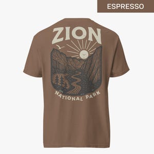 May include: A brown t-shirt with a graphic print of a mountain landscape with a sun and the text "Zion National Park".