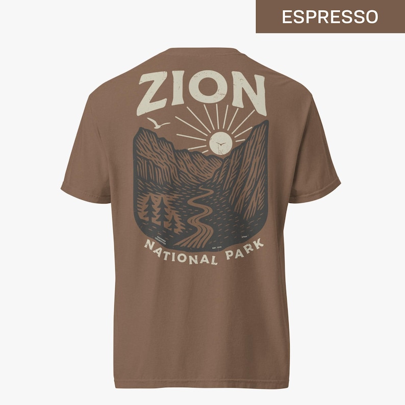 May include: A brown t-shirt with a graphic print of a mountain landscape with a sun and the text "Zion National Park".