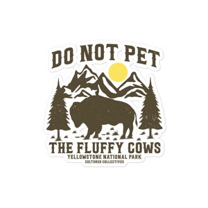 May include: A brown and white sticker with a vintage design. It features a silhouette of a bison in front of a mountain range with a yellow sun. The text "Do Not Pet The Fluffy Cows" is written in brown with the words "Yellowstone National Park" and "Cultured Collectives" in smaller text below.