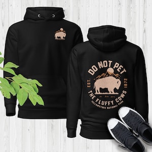 May include: Black hoodie with a brown graphic on the back that says "Do Not Pet The Fluffy Cows Est. 1872 Yellowstone National Park" and a brown silhouette of a bison. The front of the hoodie has a small brown silhouette of a bison.