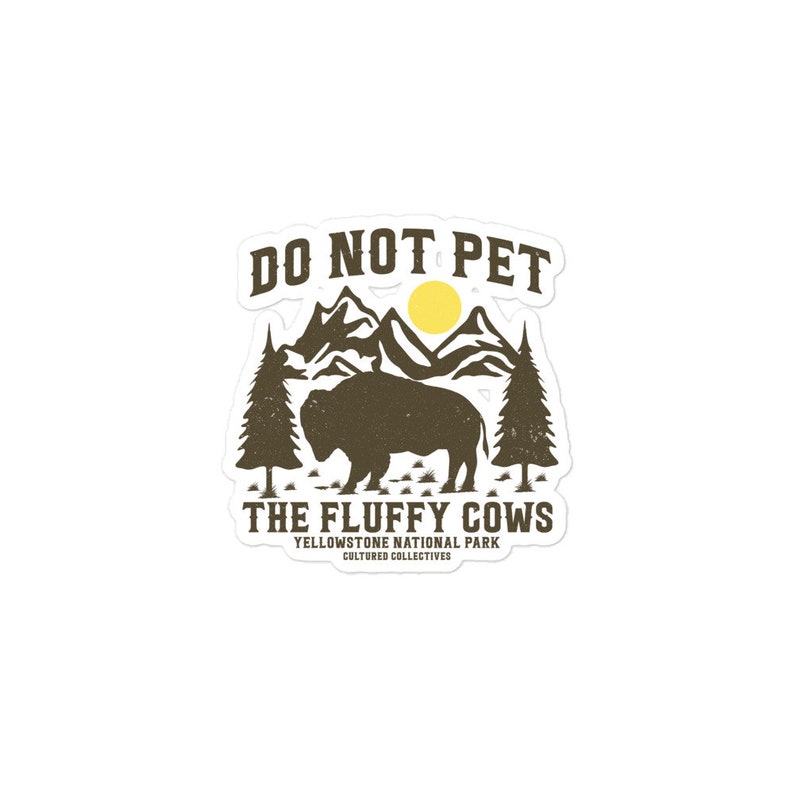 May include: A brown and white bison silhouette with a mountain range and sun behind it. The text "Do Not Pet The Fluffy Cows" is above the bison. Below the bison is the text "Yellowstone National Park" and "Cultured Collectives".