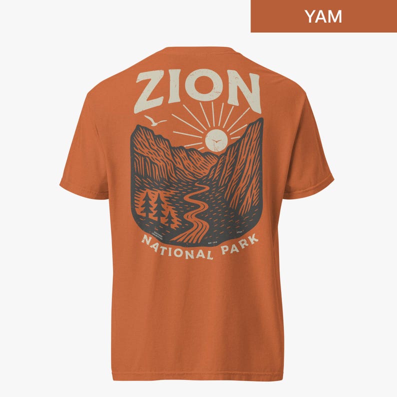May include: Orange t-shirt with a graphic print of a mountain landscape with a river, trees, and a sun. The text "Zion National Park" is printed below the graphic.